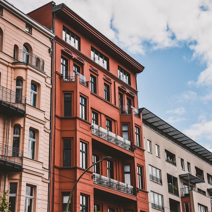 Fassade moderner Wohnhäuser mit roten und hellen Farben unter blauem Himmel.