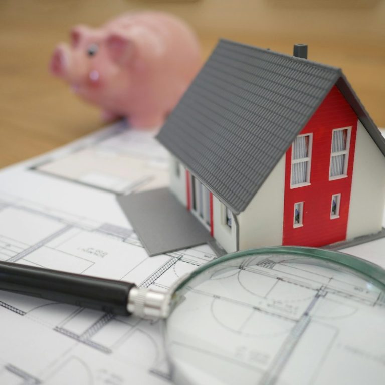 Modell eines Hauses mit einem Sparschwein und Bauplänen im Hintergrund.