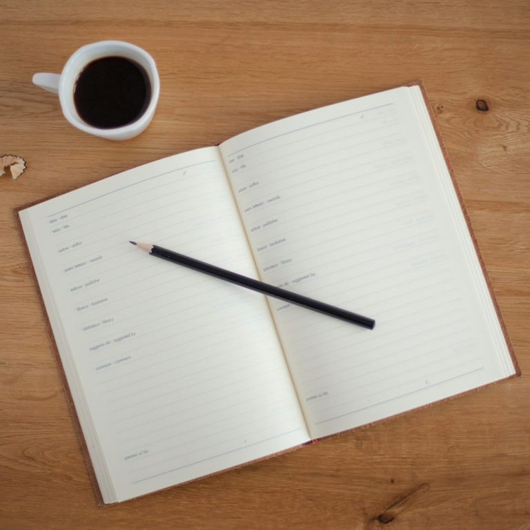 Offenes Notizbuch mit einem Bleistift und einer Tasse Kaffee auf einem Holztisch.
